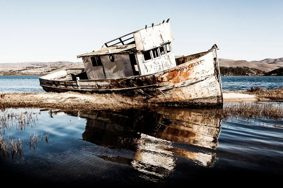 Earlier view of the Point Reyes fishing boat with its hull and leaning cabin more intact, reflected in Tomales Bay water