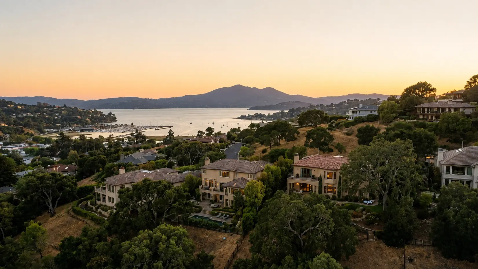 Golden-hour view from a Greenbrae hillside of bay-view homes, a marina and boats on the water, and Mount Tamalpais on the horizon