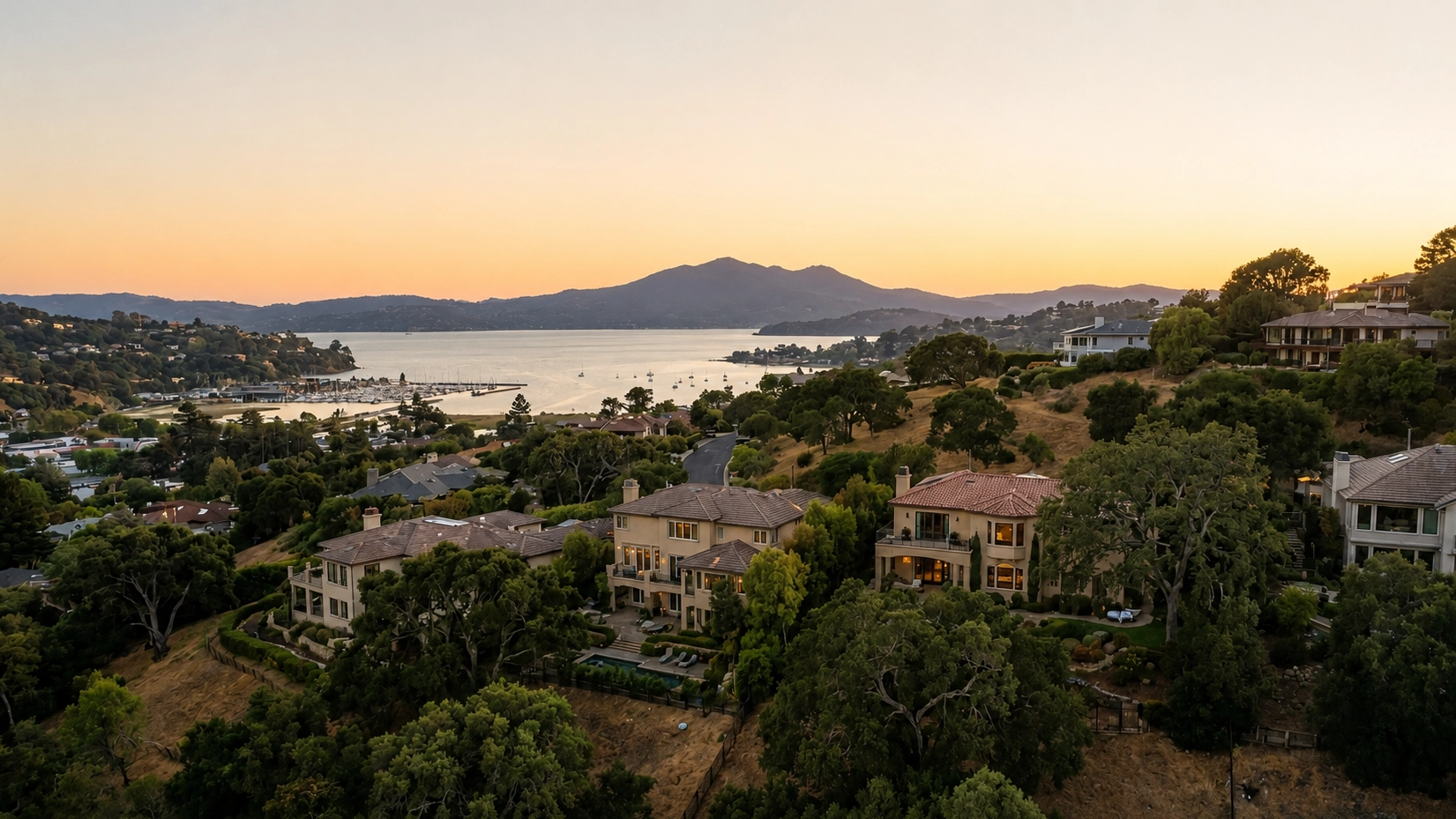 Golden-hour view from a Greenbrae hillside of bay-view homes, a marina and boats on the water, and Mount Tamalpais on the horizon
